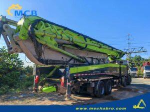 Original Mechabro field photo showing concrete pump folded boom, delivery pipework and hydraulic cylinders on a parked Zoomlion truck