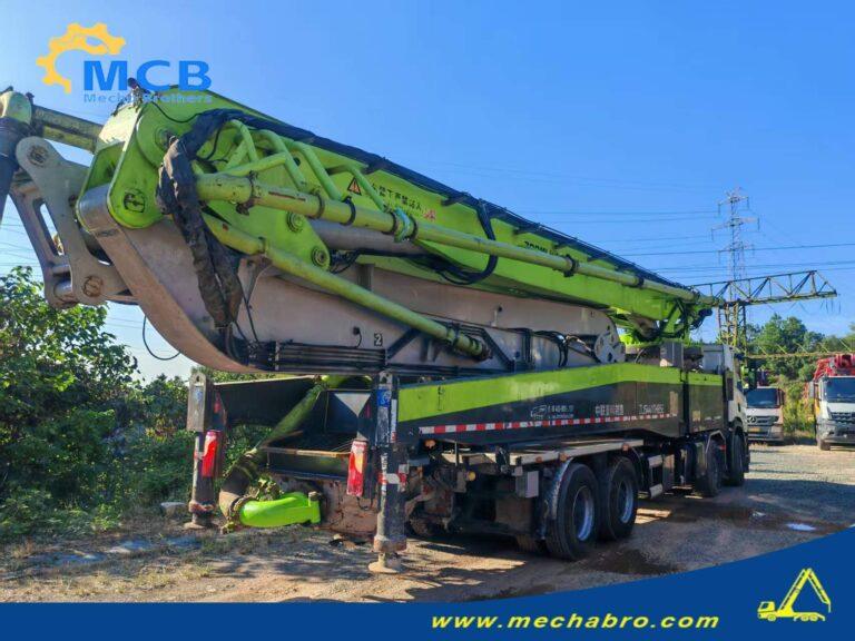 Original Mechabro field photo showing concrete pump folded boom, delivery pipework and hydraulic cylinders on a parked Zoomlion truck
